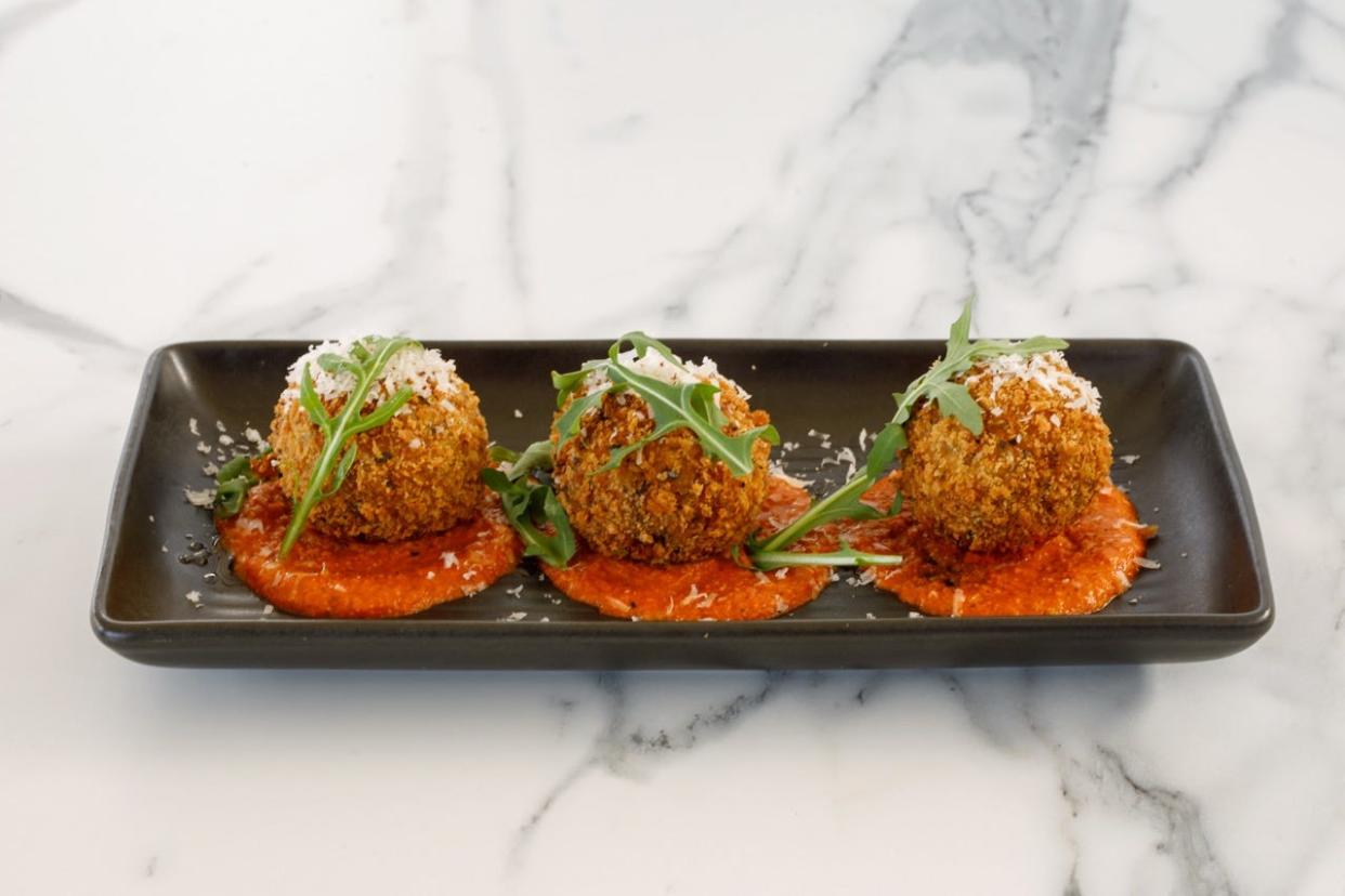 Three rice balls on rectangular plate topped with green herbs and on top of red sauce