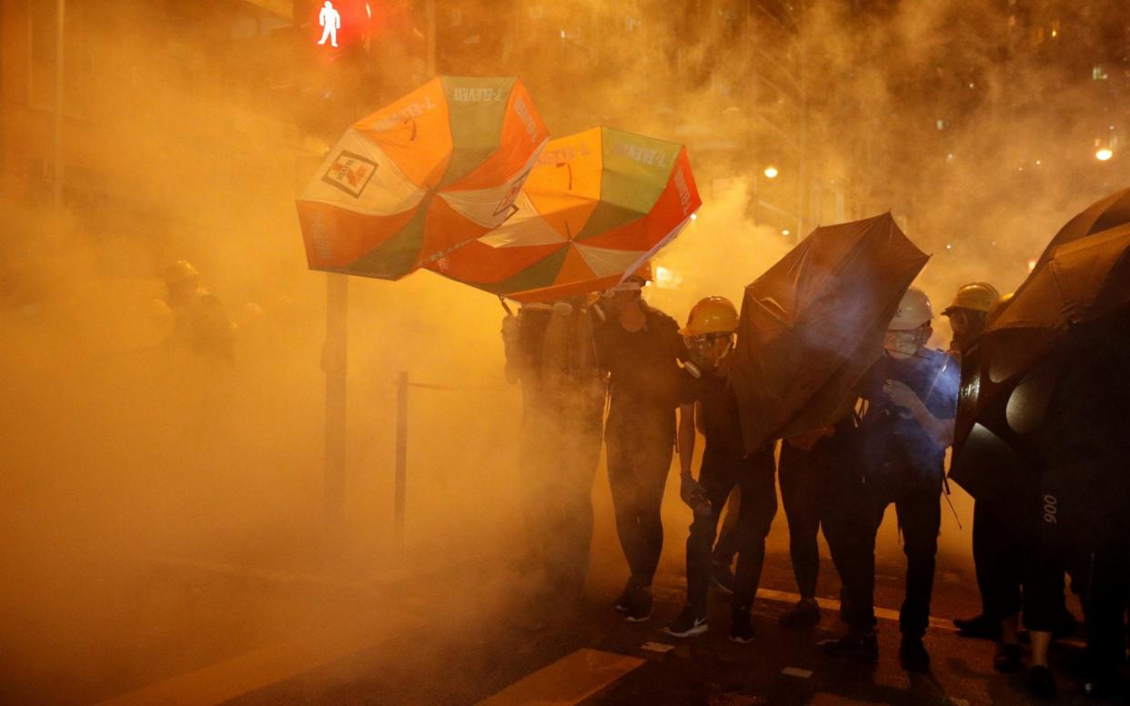 Pro-democracy protesters shield themselves with umbrellas in tear gas as they clash with police in Hong Kong - REUTERS