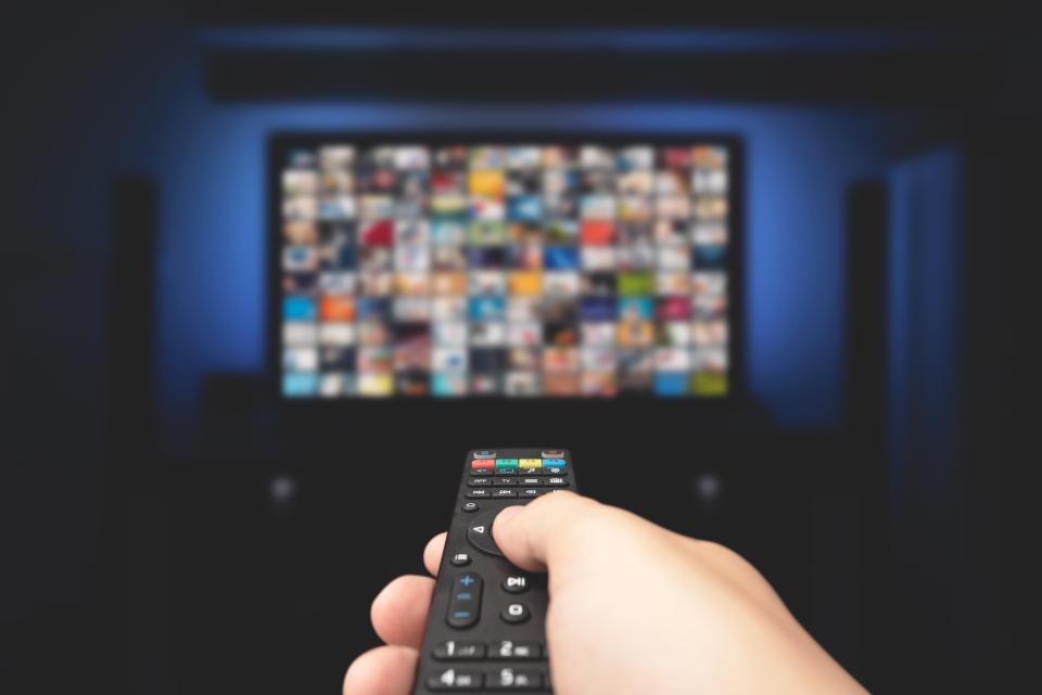 Multimedia video concept on TV set in dark room. Man watching TV with remote control in hand.