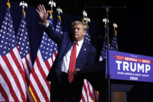 Donald Trump waving to audience with U.S. flags behind him.