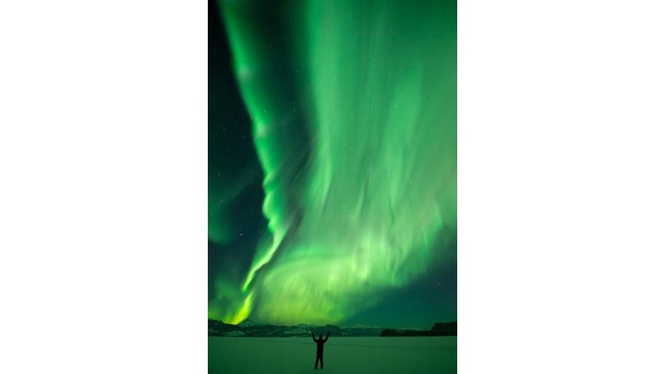 A silhouetted figure stands beneath an incredible northern lights display over Lake Laberge in Yukon.