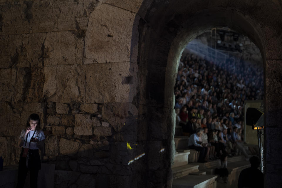 A festival staff member checks her phone as spectators watch a performance of "Madame Butterfly" at the Odeon of Herodes Atticus in Athens, on Thursday, June 1, 2023. The annual arts festival in Athens and at the ancient theater of Epidaurus in southern Greece is dedicated this year to the late opera great Maria Callas who was born 100 years ago. (AP Photo/Petros Giannakouris)