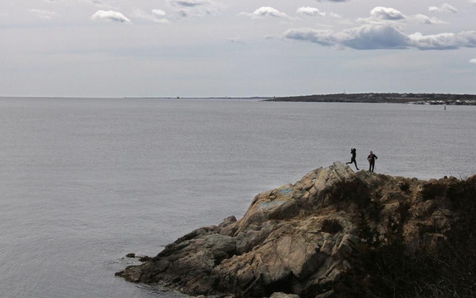 A couple navigate the rocks on an overcast day at Fort Wetherill State Park, Jamestown.