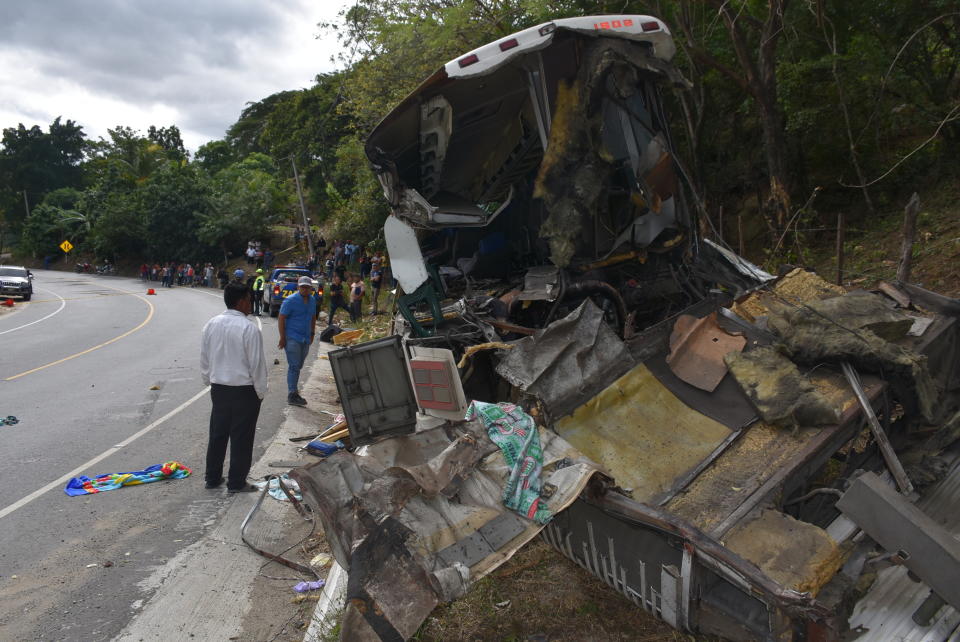 The wreckage of a passenger bus that crashed with a trailer truck lays on the side of the highway in Gualan, Guatemala, Saturday, Dec. 21, 2019. The early morning accident killed at least 21 people and left a dozen wounded, according to the national disaster agency. (AP Photo/Carlos Cruz)