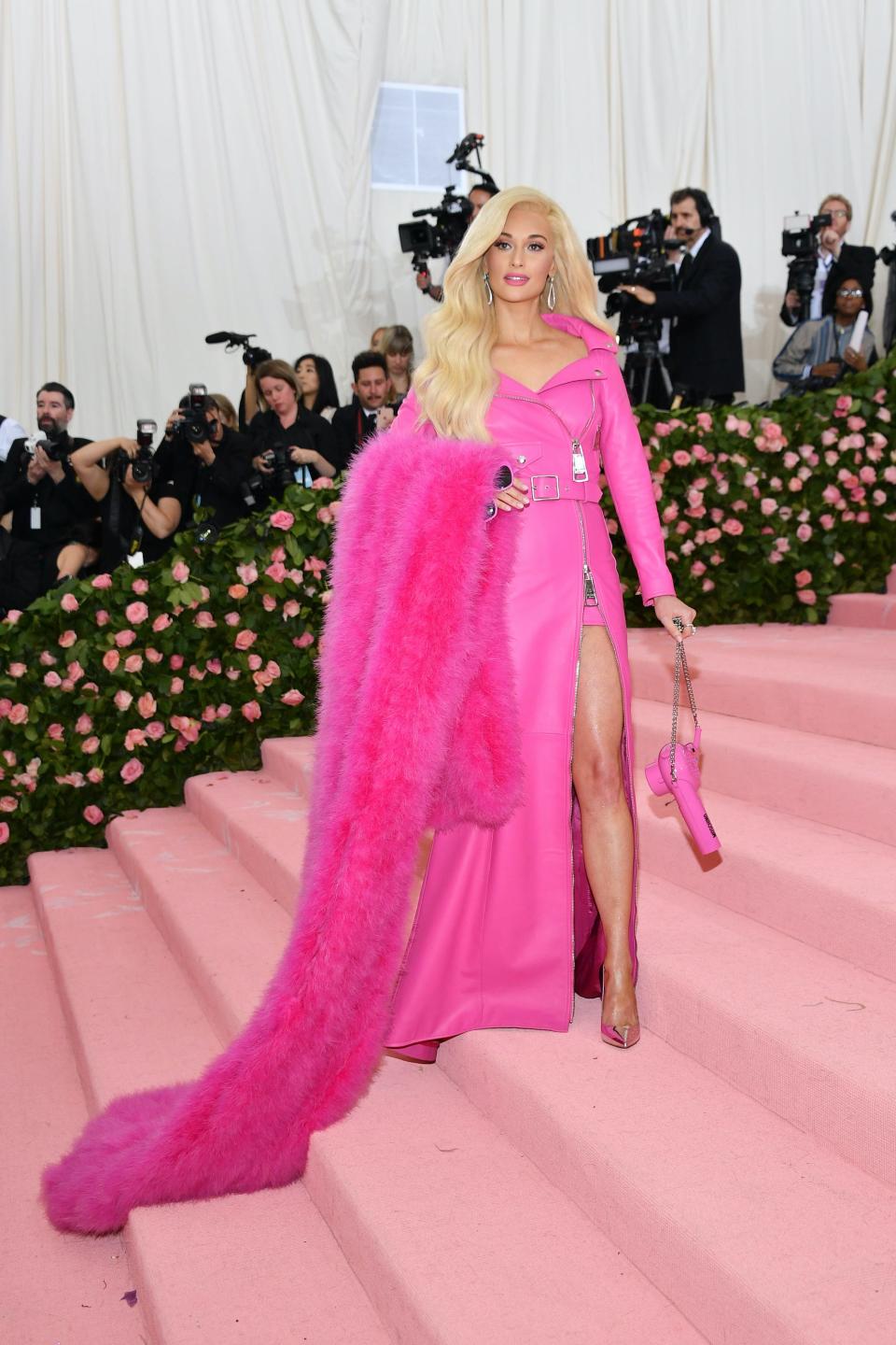 Kacey Musgraves at the 2019 Met Gala with blonde hair and in a bright pink dress with a fur stole on her arm.