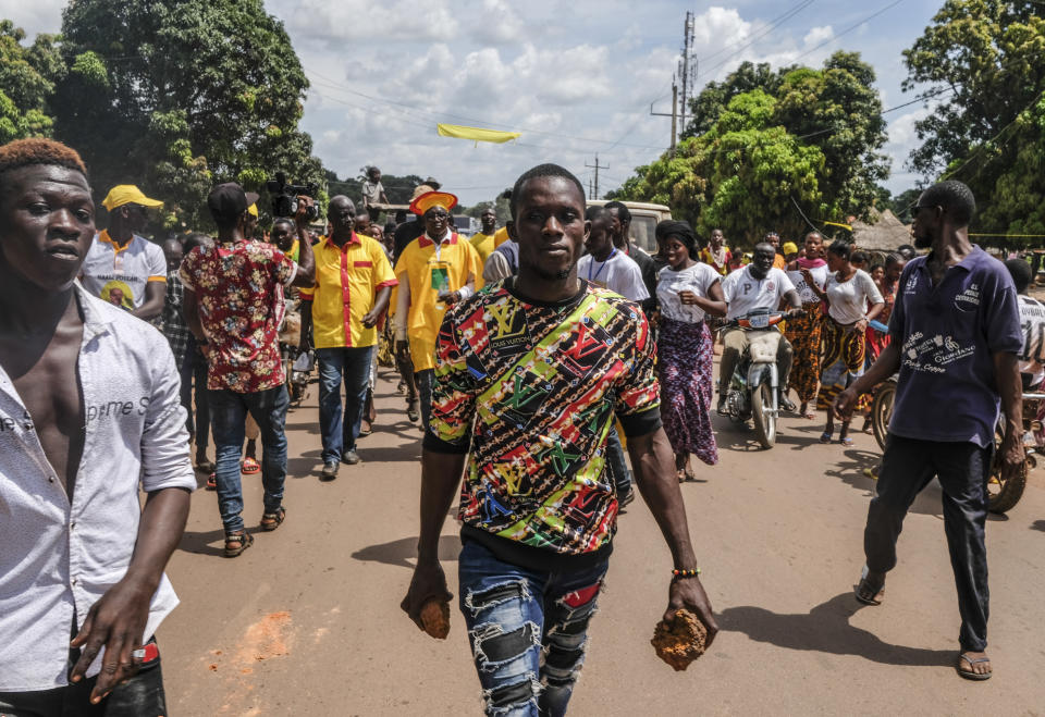 A supporter of the ruling Rally of the Guinean People (RPG) party holds rocks as he and others demonstrate against the opposition Union of Democratic Forces of Guinea (UFDG) party and to block the visit of their leader, in the streets of Kankan, Guinea Sunday, Oct. 11, 2020. The stage is set for Oct. 18 presidential elections pitting incumbent President Alpha Conde, 82, who is bidding for a third term, against opposition leader Cellou Dalein Diallo, who was previously defeated by Conde in both the 2010 and 2015 elections. (AP Photo/Sadak Souici)