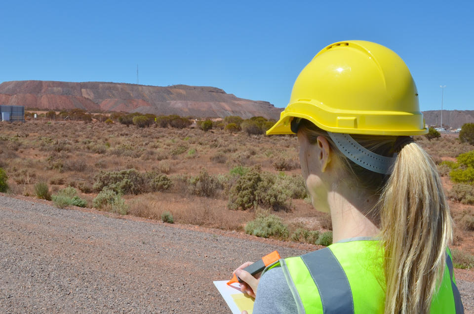 A woman in a hard hat with a notebook overlooking a potential mine site.