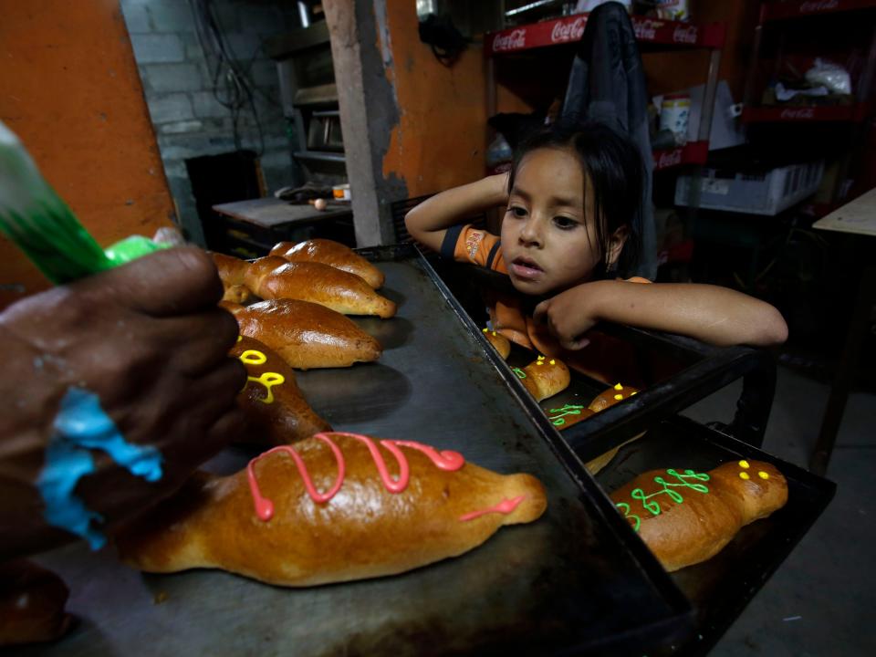 Emily watches her grandfather Francisco Guachamin decorate 'Guaguas de pan' or bread babies in his bakery in Llano Chico, Ecuador, Thursday, Oct. 31, 2013. The sweet bread that is usually shaped in the form of a swaddled infant or small child is traditionally eaten during Day of the Dead celebrations. Guagua is the Quechua word for baby or toddler. And pan is the Spanish word for bread.