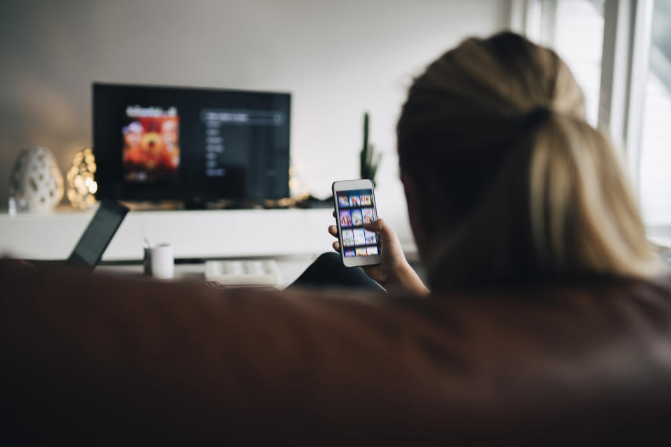 A girl using her smart phone to change TV channel