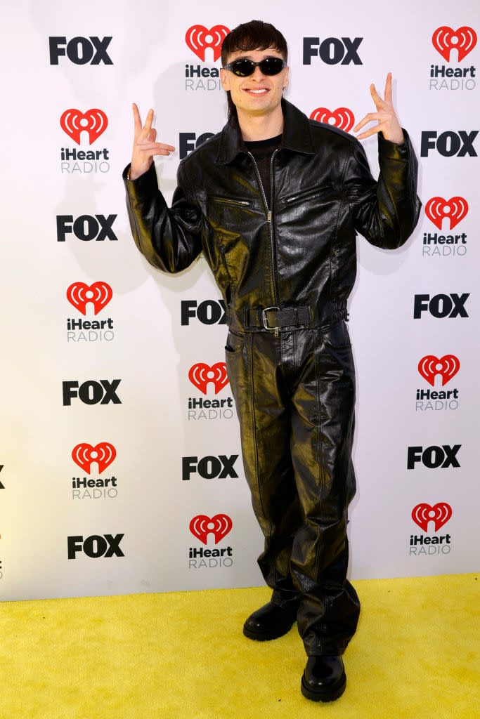 Person in a black leather outfit with jacket and trousers, making peace signs, at iHeart Radio event