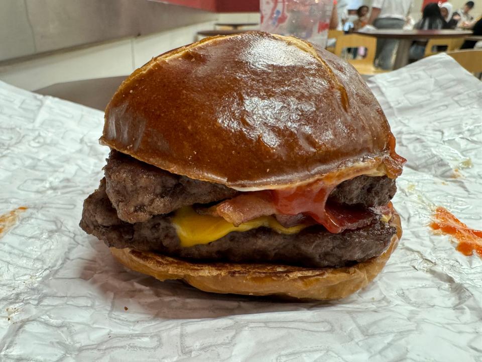 Side view of a large burger with a pretzel bun, two patties, cheese slices, and ketchup on a table at Wendy's