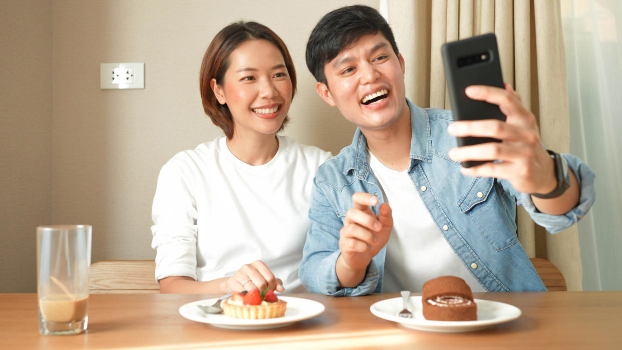 close up group of asian lover sitting in dining room to talking with happiness and use smartphone to take picture and upload on social media application for lifestyle in vacation concept