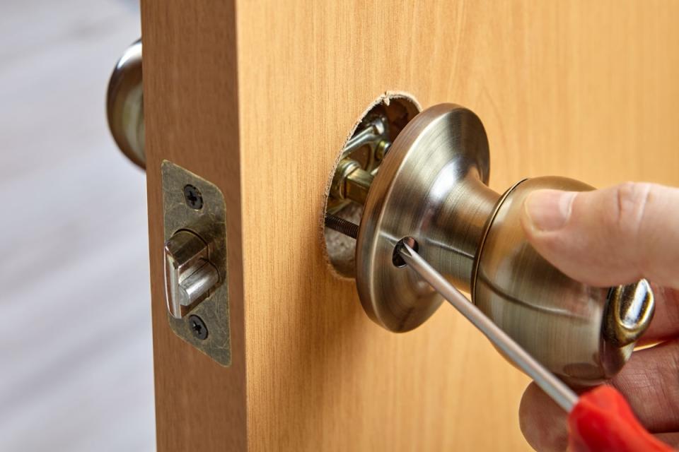 Person using screwdriver to unscrew and remove a door knob.