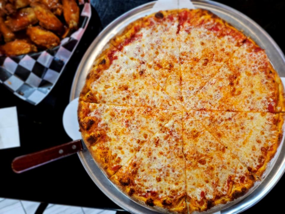 A large cheese pizza at Agrigento Pizzeria Caffe in Bradenton photographed with an order of their chicken wings in the background on Dec. 10, 2023.