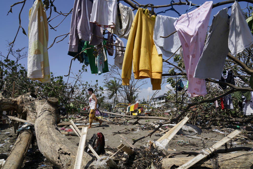 A woman walks past clothes that are left to dry on toppled trees due to Typhoon Rai in Talisay, Cebu province, central Philippines on Saturday Dec. 18, 2021. A strong typhoon engulfed villages in floods that trapped residents on roofs, toppled trees and knocked out power in southern and central island provinces, where more than 300,000 villagers had fled to safety before the onslaught, officials said. (AP Photo/Jay Labra)