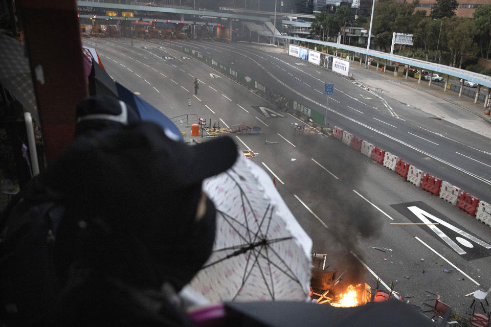 A protester watches as a fire burns amid debris placed to block a road leading to the Cross-Harbour Tunnel in Hong Kong, Thursday, Nov. 14, 2019. University students from mainland China and Taiwan are fleeing Hong Kong, while those from three Scandinavian countries have been moved or urged to leave as college campuses become the latest battleground in the city's 5-month-long anti-government unrest. (AP Photo/Ng Han Guan)