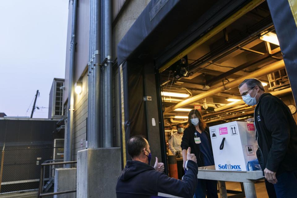 A FedEx driver gives a thumbs up after delivering a box containing the Pfizer-BioNTech COVID-19 vaccine to pharmacists Richard Emery, right, and Karen Nolan as it arrives at Rhode Island Hospital in Providence, R.I, Monday, Dec. 14, 2020.<span class="copyright">David Goldman–AP</span>