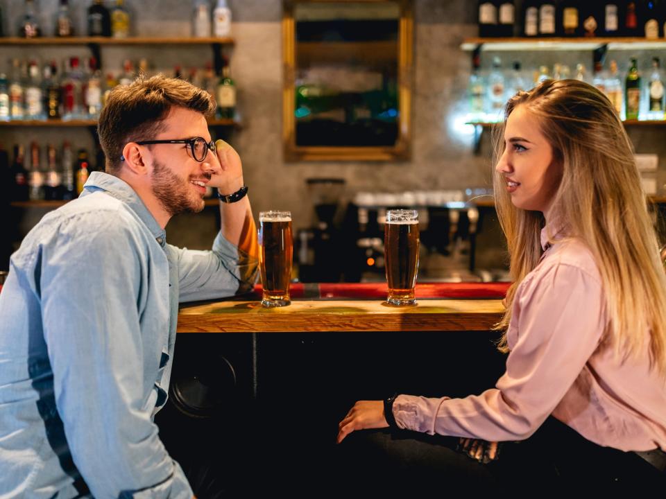 Young Caucasian man and woman having their first date in a pub, drinking beer and talking.