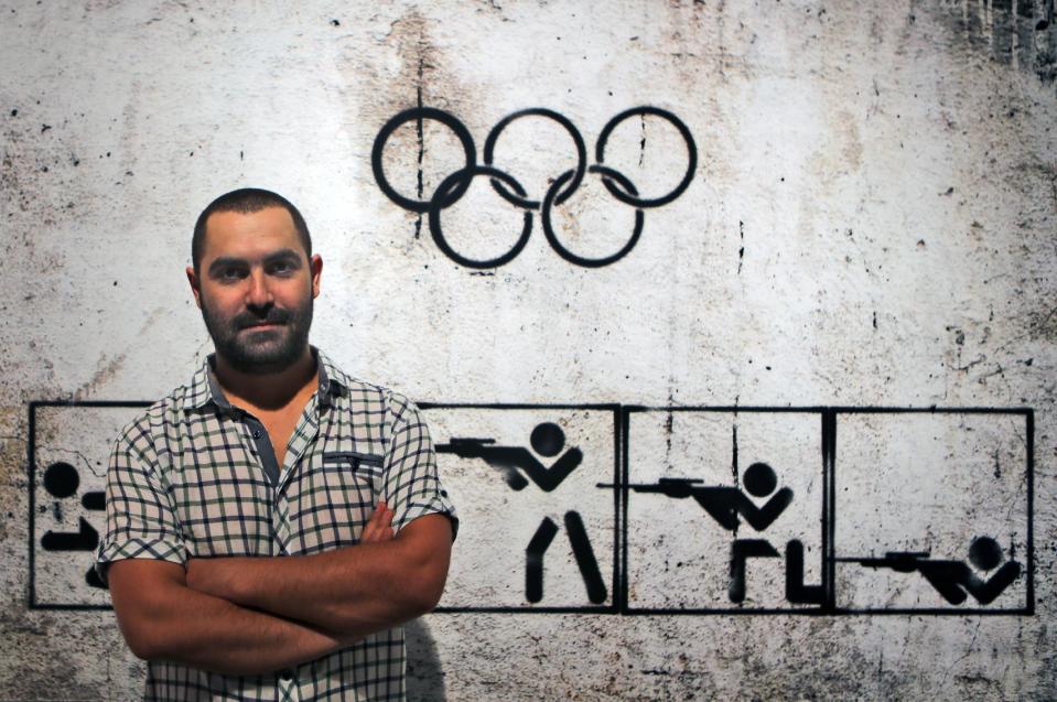 In this Monday, Sept. 16, 2013 photo, Syrian artist Tammam Azzam, 23, poses in front of one of his works, a digital print titled "Syrian Olympic" during the Young Collectors Auction at Ayyam gallery in Dubai, United Arab Emirates. The auction Monday in Dubai's evolving art district _ tucked inside an industrial zone of warehouses and businesses _ served as a window into a small but forward-looking effort to save one niche of Syria's artistic community with no end in sight to the civil war that has already claimed more than 100,000 lives.(AP Photo/Kamran Jebreili)