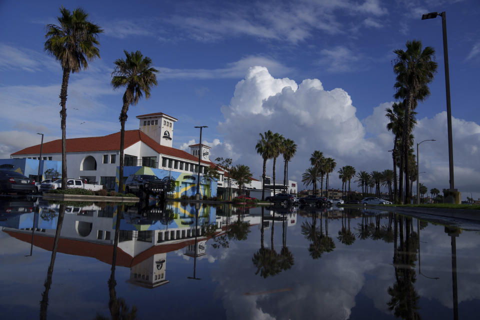 A flooded parking lot reflects palm trees, Thursday, Feb. 1, 2024, in Huntington Beach, Calif. Heavy rain flooded California roadways and much-needed snow piled up in the mountains as the first of back-to-back atmospheric rivers pummeled the state Thursday, Feb. 1, 2024. (AP Photo/Eric Thayer)