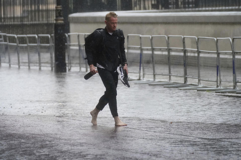 A man walks in bare feet through flood water in Horse Guards Road in central London, Sunday July 25, 2021. Thunderstorms bringing lightning and torrential rain to the south are set to continue until Monday it is forecast. (Victoria Jones/PA via AP)