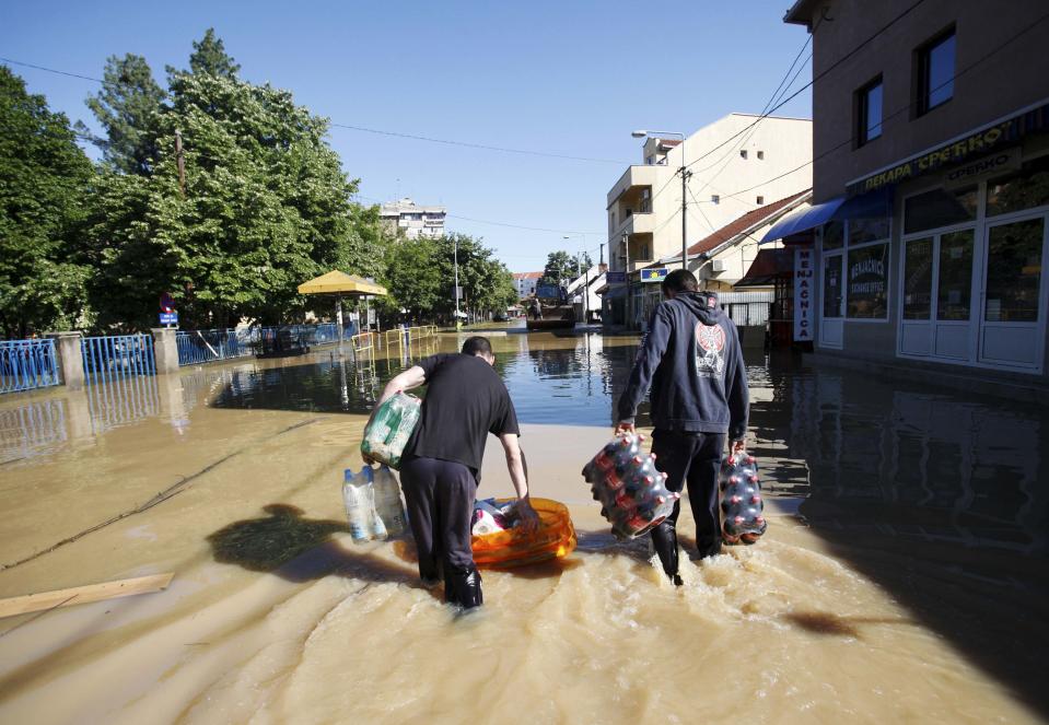 Local youths walk through flood waters with items they looted from a store in the town of Obrenovac