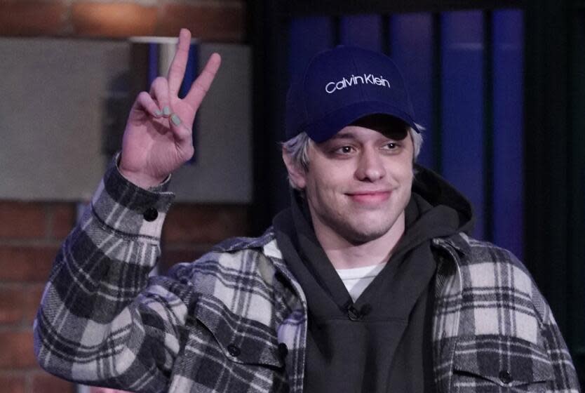 A man wearing a plaid shirt and blue Calvin Klein hat while flashing a peace sign