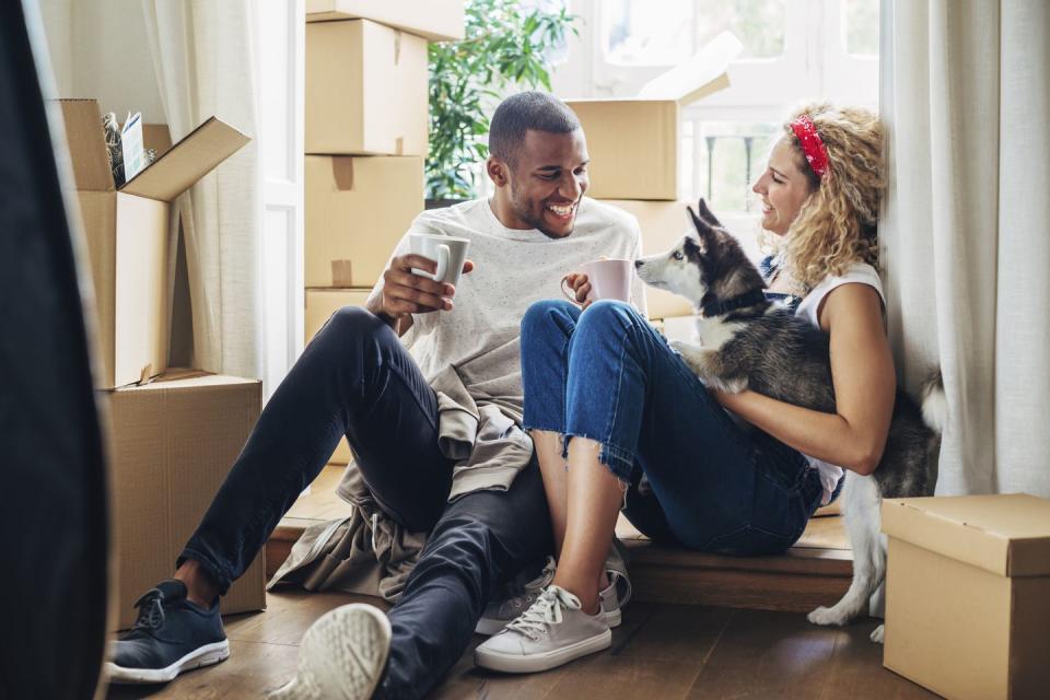 happy couple playing with dog while sitting at doorway in new house