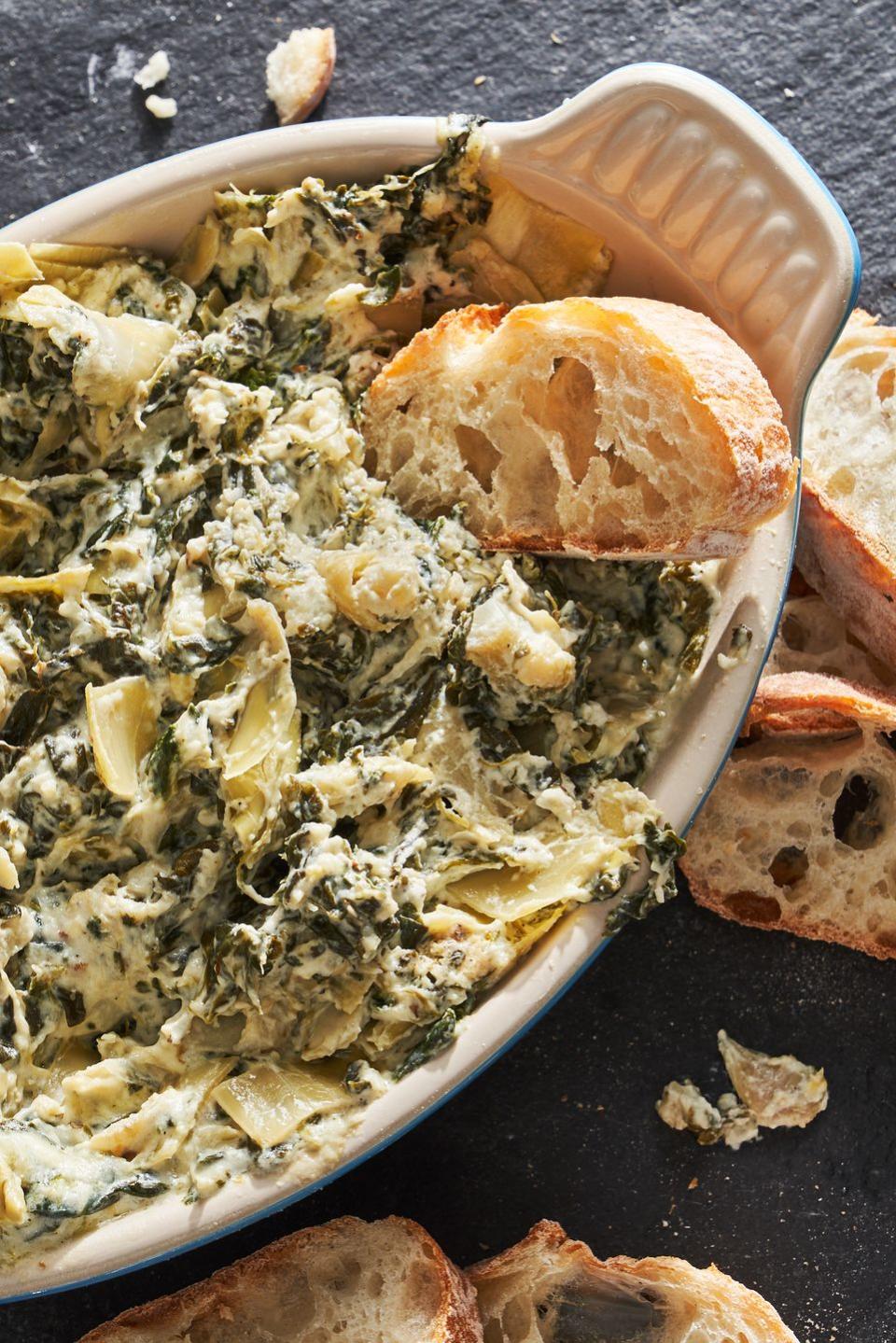 crock pot spinach and artichoke dip in a blue dish surrounded by slices of bread