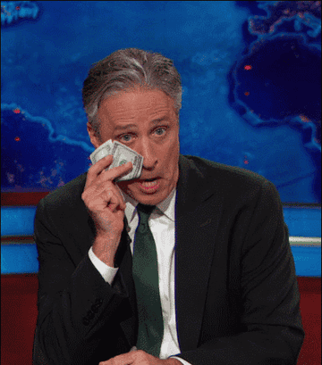 John Stewart holding a $100 bill.