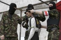 Masked pro-Russia insurgents show a detained man, who reportedly is a member of the Right Sector, a nationalist Ukrainian group, when people gathered at barricades in front of a regional administration building that was seized by pro-Russian activists earlier in Donetsk, Ukraine, Sunday, April 20, 2014. The Ukrainian and Russian governments are reporting a shootout at a checkpoint set up by pro-Russian insurgents in eastern Ukraine that has left one person dead and others hospitalized with gunshot wounds. Pro-Russian activists brought to the stage a man who was accused of being a member of the radical organization Right sector. They also spoke about what he had found weapons and ammunition.(AP Photo/Max Vetrov)