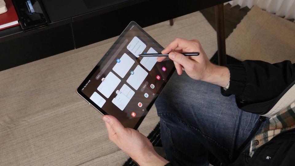 A man looks at different apps on the Samsung Galaxy Tab S8, holding the S Pen.
