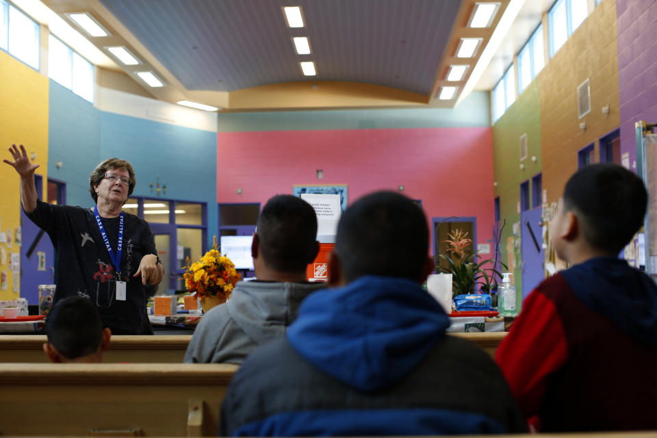 In in this Feb. 21, 2020 photo, volunteer Susan Gallegos talks to newly arrived asylum seekers from Central America at Casa Alitas, a Catholic-run shelter in Tucson, Ariz. For years, Catholic-led, U-S.-based nonprofits have been at the forefront of efforts to support migrants and asylum seekers along the Mexican border. Tough new border policies, coupled with the COVID-19 pandemic, have drastically changed their work, much of which now takes place in Mexico. (AP Photo/Dario Lopez-MIlls)