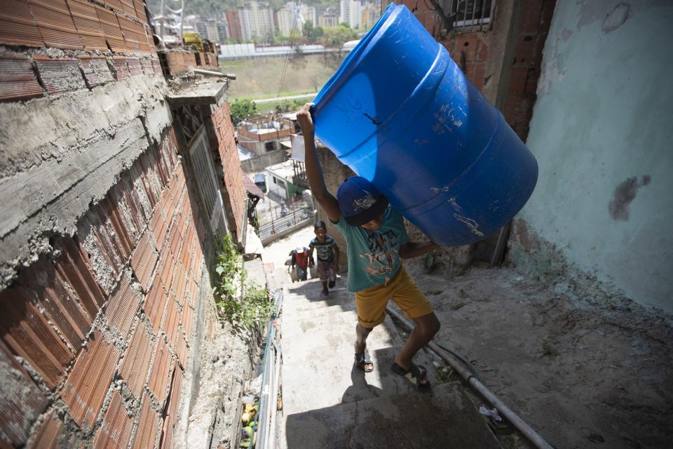 Un niño sube unas escaleras cargado con dos recipientes vacíos que llenará con el agua suministrada por un camión cisterna del gobierno, en el vecindario de Petare, en Caracas, Venezuela, el 15 de junio de 2020. El colapso económico de Venezuela ha dejado a la mayoría de los hogares sin un suministro de agua corriente confiable. (AP Foto/Ariana Cubillos)