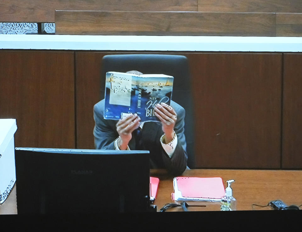 Darrell Brooks appears on a video screen in an adjacent courtroom as he hides his face behind a Holy Bible after being removed from the court after repeated interruptions during his trial in a Waukesha County Circuit Court in Waukesha, Wis., on Monday, Oct. 24, 2022. Brooks, who is representing himself during the trial, is charged with driving into a Waukesha Christmas Parade last year, killing six people and injuring dozens more. (Mike De Sisti/Milwaukee Journal-Sentinel via AP, Pool)