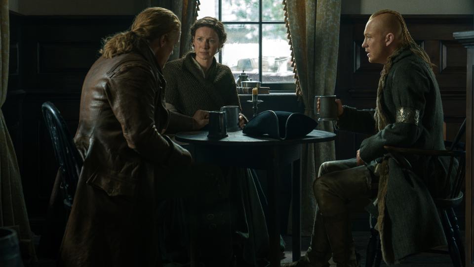 Jamie Fraser, Claire Fraser and Young Ian sit at an inn table in Outlander season 7