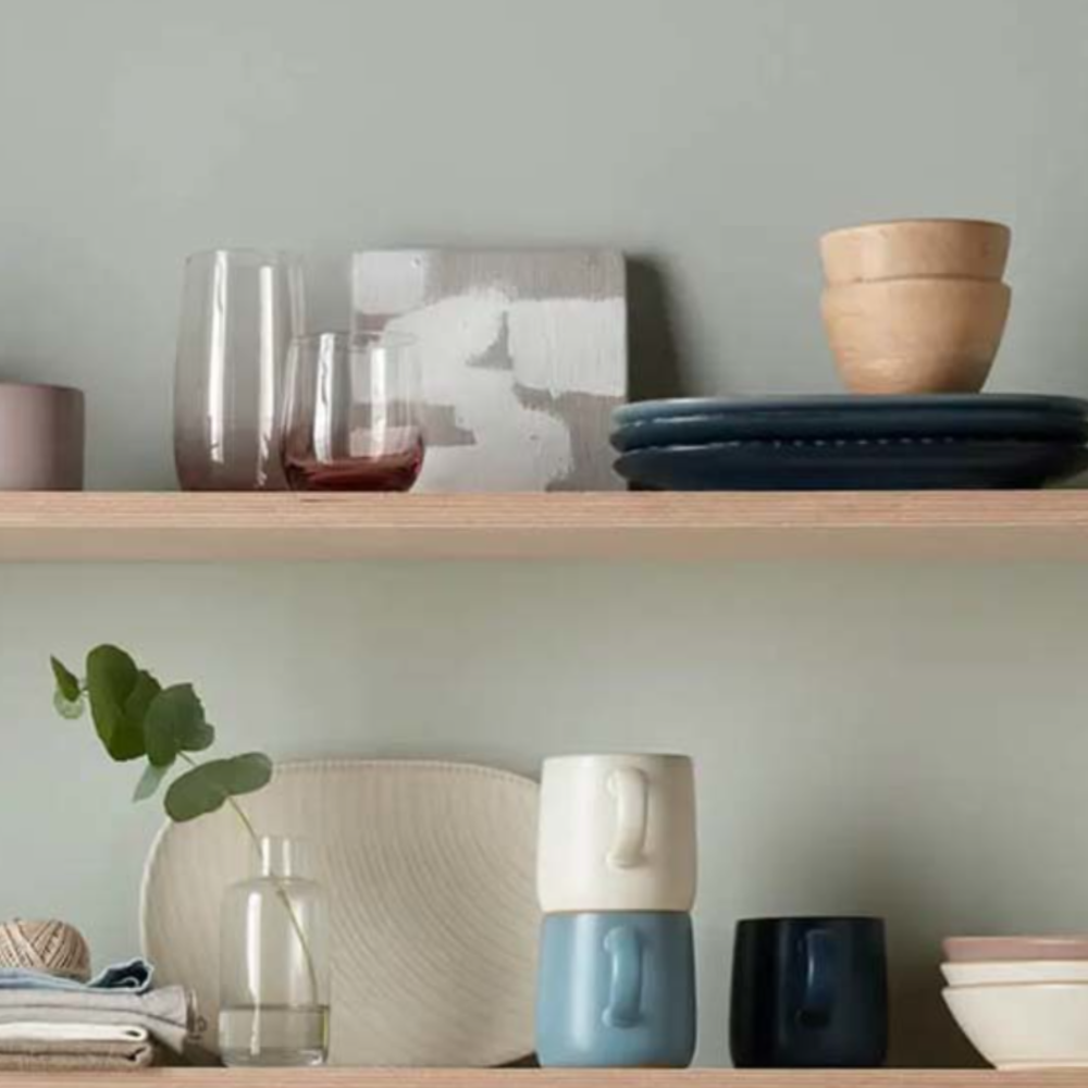  Kitchenware and mugs on a shelf with pale green wall. 