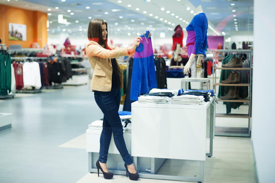 A woman holds up a shirt to examine while shopping in a clothing store.