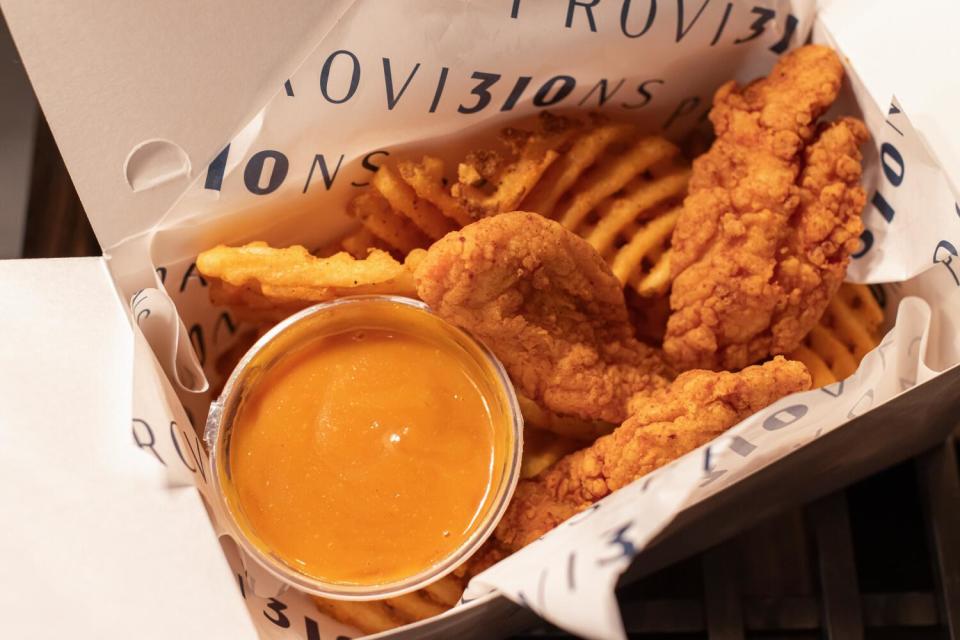 Chicken tenders and waffle fries in a cardboard with a cup of yellow dipping sauce