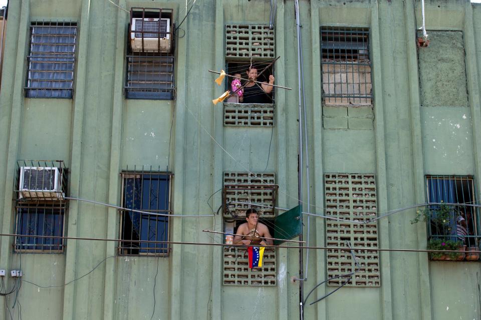 In this photo taken on Saturday, March 15, 2014. Residents look out from their apartments at a opposition protest at Isabelica neighborhood outside Valencia , Venezuela. The people of the poor district of La Isabelica were made to pay for taking to the streets in anti-government protests. More than a dozen masked men on motorcycles roared through, shooting up a barricade and killing a university student and a 42-year-old man painting his house. (AP Photo/Fernando Llano)