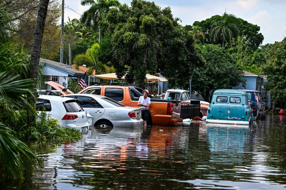 Cars in water midway up their tires, as one person leans against a truck