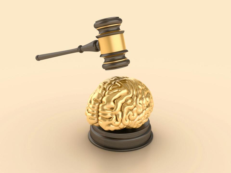 A tiny golden brain, about to hit by a wooden gavel with a gold band on it.