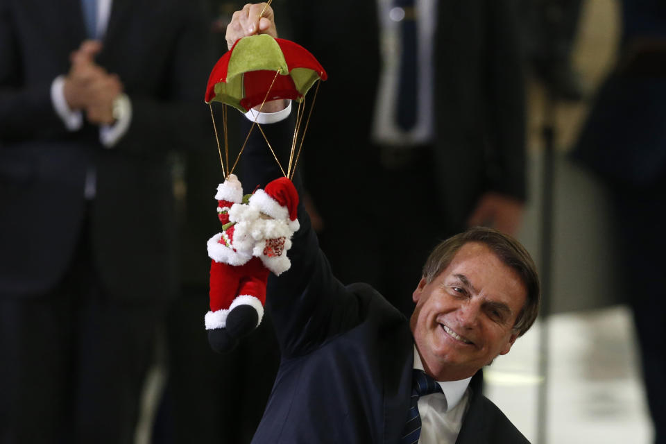 Brazil's President Jair Bolsonaro holds Santa Claus doll on a parachute, during the Christmas celebration with staff and students at the Planalto Presidential Palace, in Brasilia, Brazil, Thursday, Dec. 19, 2019. (AP Photo /Eraldo Peres)