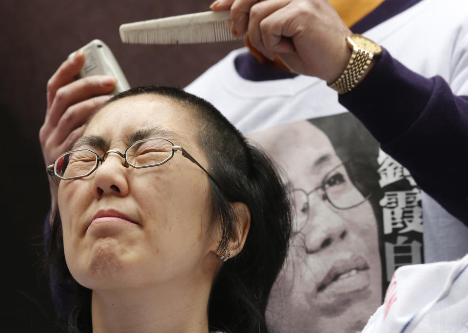 A pro-democracy protester shaves her head next to a T-shirt printed a portrait of Liu Xia, the detained wife of Chinese Nobel Peace laureate Liu Xiaobo during a demonstration in Hong Kong Friday, Feb. 14, 2014 as they demanded Chinese government to release Liu Xia from house arrest. The T-shirt reads "Release Liu Xia." (AP Photo/Kin Cheung)