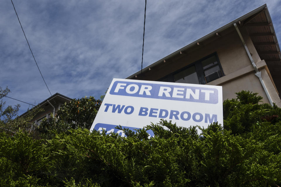 Sign reads "FOR RENT TWO BEDROOM" in front of a residential building with greenery