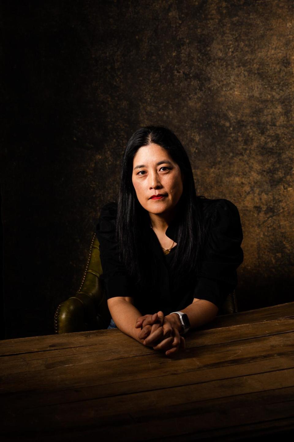 Victoria Chang sits at a table with her hands folded on it.