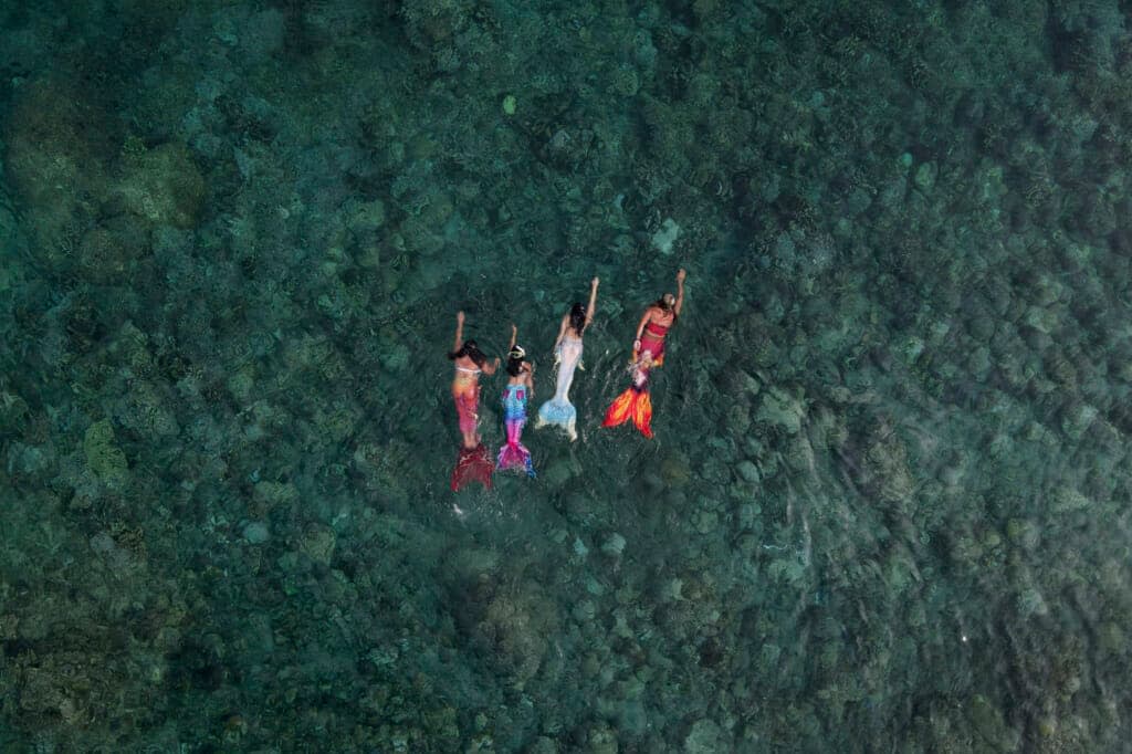 Queen Pangke Tabora, right, swims with her students, from left, Shelah Candado, Jennica Secuya and Meryll Louise Reque, during a mermaiding class in Mabini, Batangas province, Philippines on Sunday, May 22, 2022. (AP Photo/Aaron Favila)