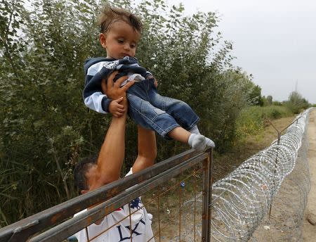 A Syrian Kurdish migrant holds a girl on the Hungarian-Serbian border near Asotthalom, Hungary August 25, 2015. REUTERS/Laszlo Balogh