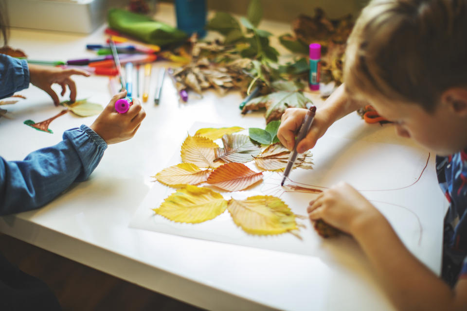 Children crafting with autumn leaves on a table, using markers and glue for a DIY project