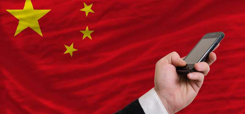 Hand holding a cell phone in front of the Chinese flag.